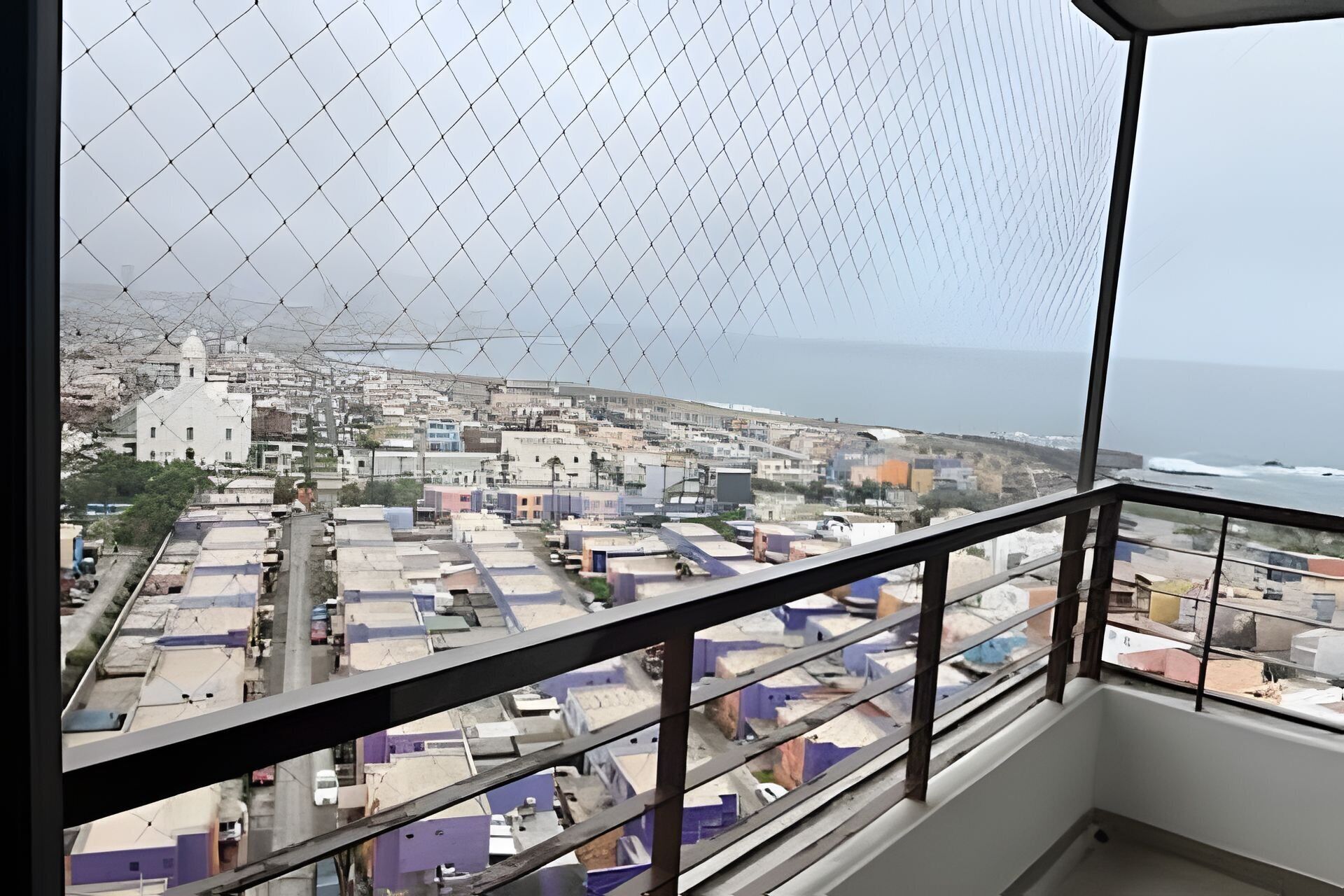 Un balcón con vistas a un paisaje urbano costero, que incluye edificios y el mar.