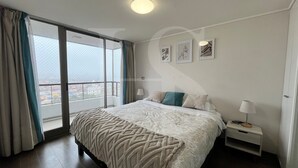 A hotel room with a large bed, a nightstand, a window with curtains, and artwork on the wall.