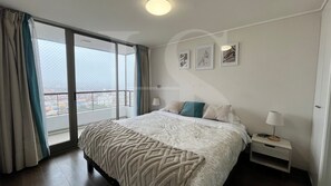 Una habitación de hotel con una cama grande, una mesita de noche, una ventana con cortinas y una obra de arte en la pared.