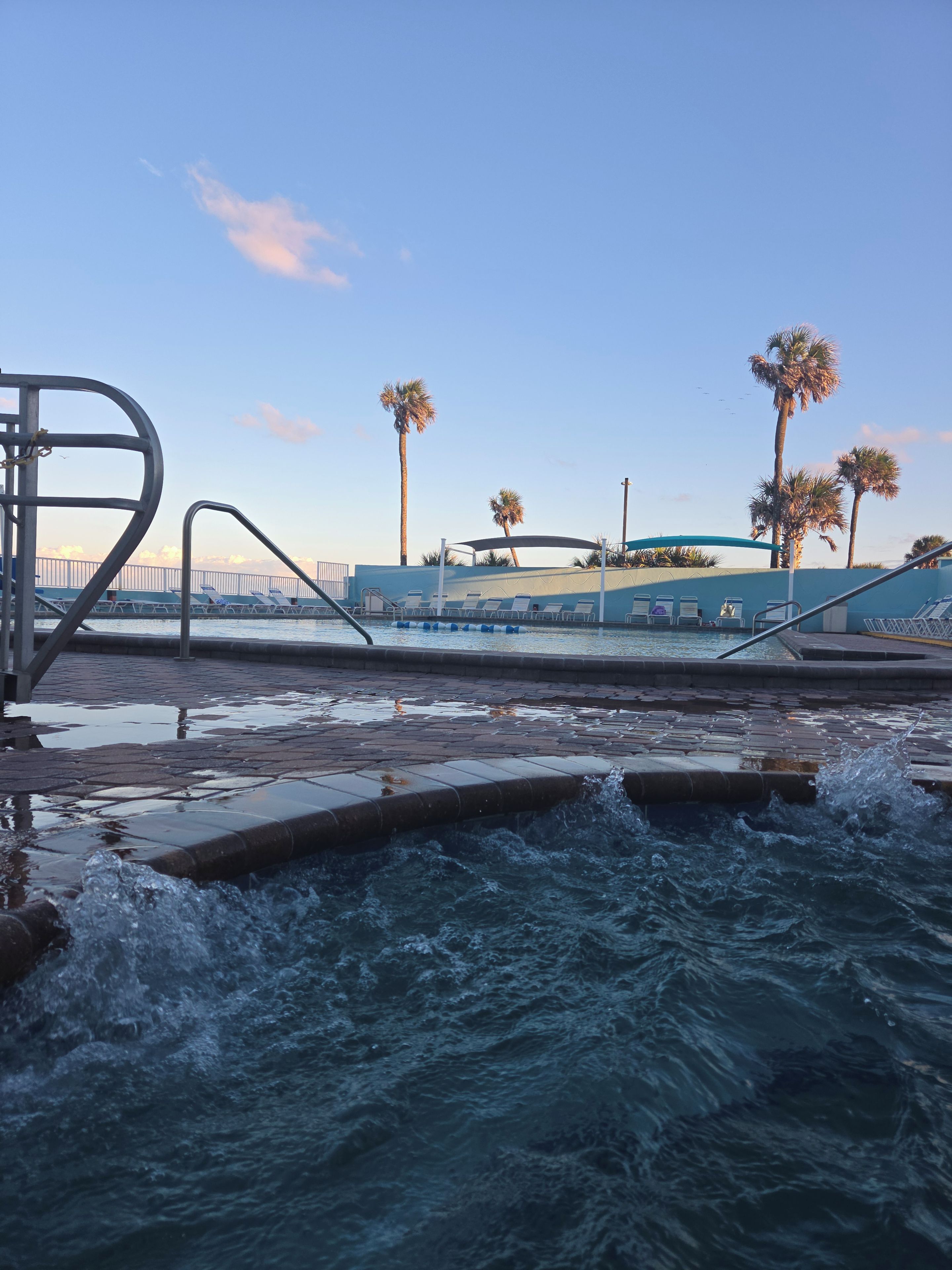 A pool area with water jets, lounge chairs, and palm trees.
