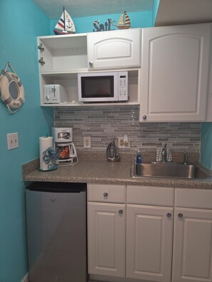 A compact kitchen with white cabinets, a built-in microwave, a sink, and a dishwasher. - Oceanfront Paradise at Fountain Beach Resort / Daytona Beach (Daytona Beach)