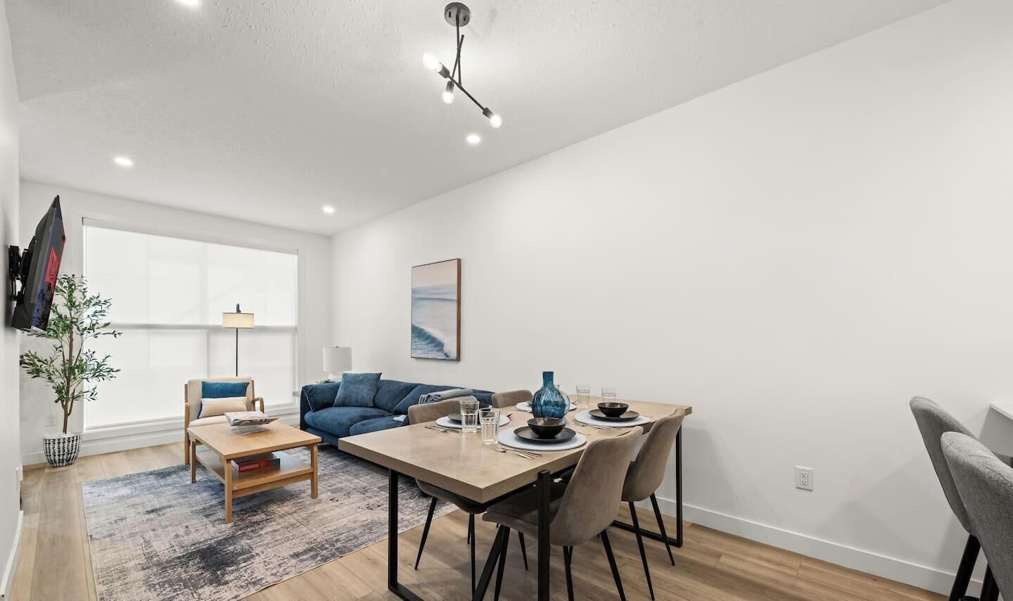 A modern living room with a dining area, a sofa, a coffee table, and a TV mounted on the wall.