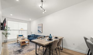 A modern living room with a dining area, a sofa, a coffee table, and a TV mounted on the wall.