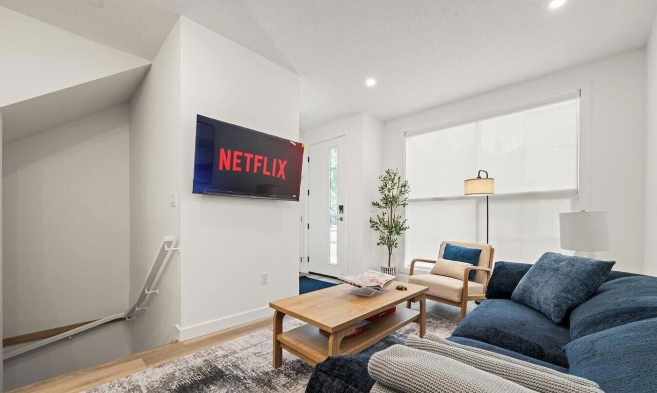 En moderne stue med et fladskærms-tv på væggen, et træsofabord, en blå sofa og en gulvlampe.