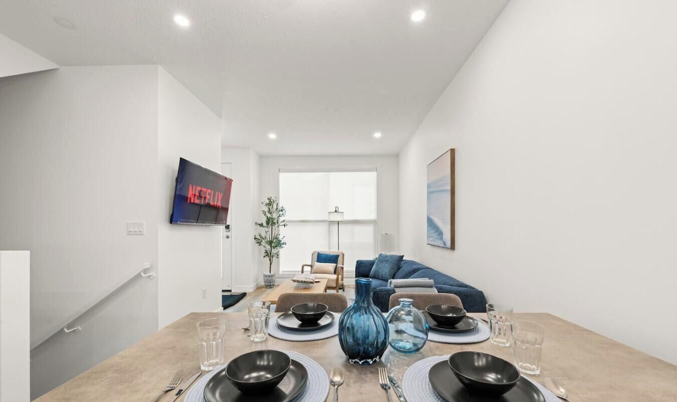 A modern dining area with a table set for four, a blue vase, and a television displaying 'Netflix' in the background.