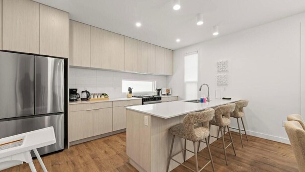 A modern kitchen with a stainless steel refrigerator, a central island with bar stools, and light wood cabinetry. - Air | Bright 2BR Near Downtown & WEM | 2 King Beds (Edmonton)