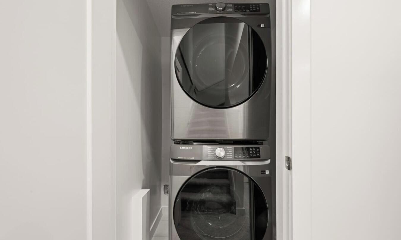 Une machine à laver et un sèche-linge superposés dans une pièce aux murs blancs.