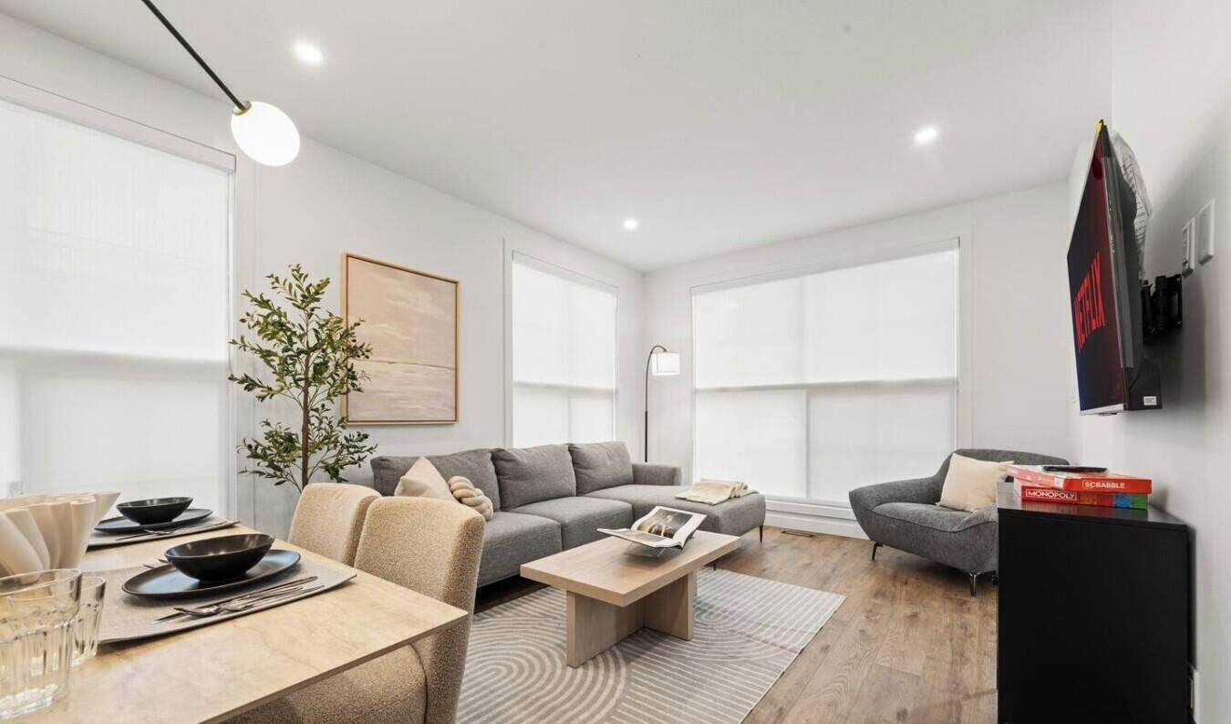 A modern living room with a sofa, armchairs, a coffee table, and a dining area with chairs and plates.