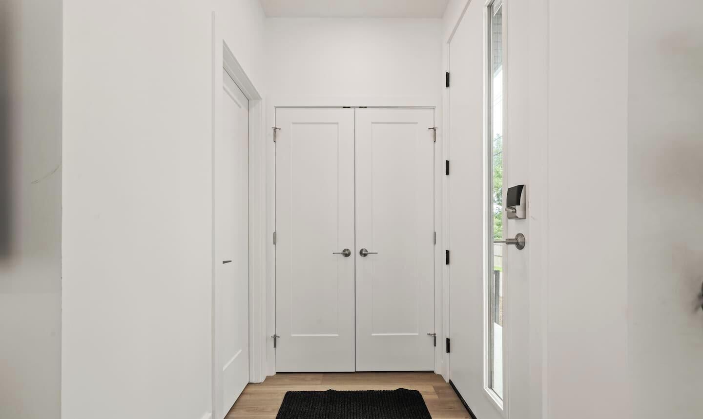A hallway with a double door, a black rug on the floor, and a window on the right side.