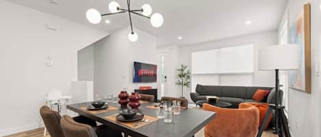 Un espacio de estar moderno con comedor, sofá, lámpara y televisor.