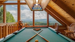 Ein Billardtisch in einem Raum mit großen Fenstern und Bergblick.