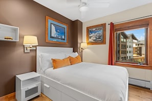 A bedroom with a bed, nightstands, a window with a view of buildings, and two wall-mounted lamps. - Scenic Mountain Sanctuary Steps from Keystone Gondola (Keystone)