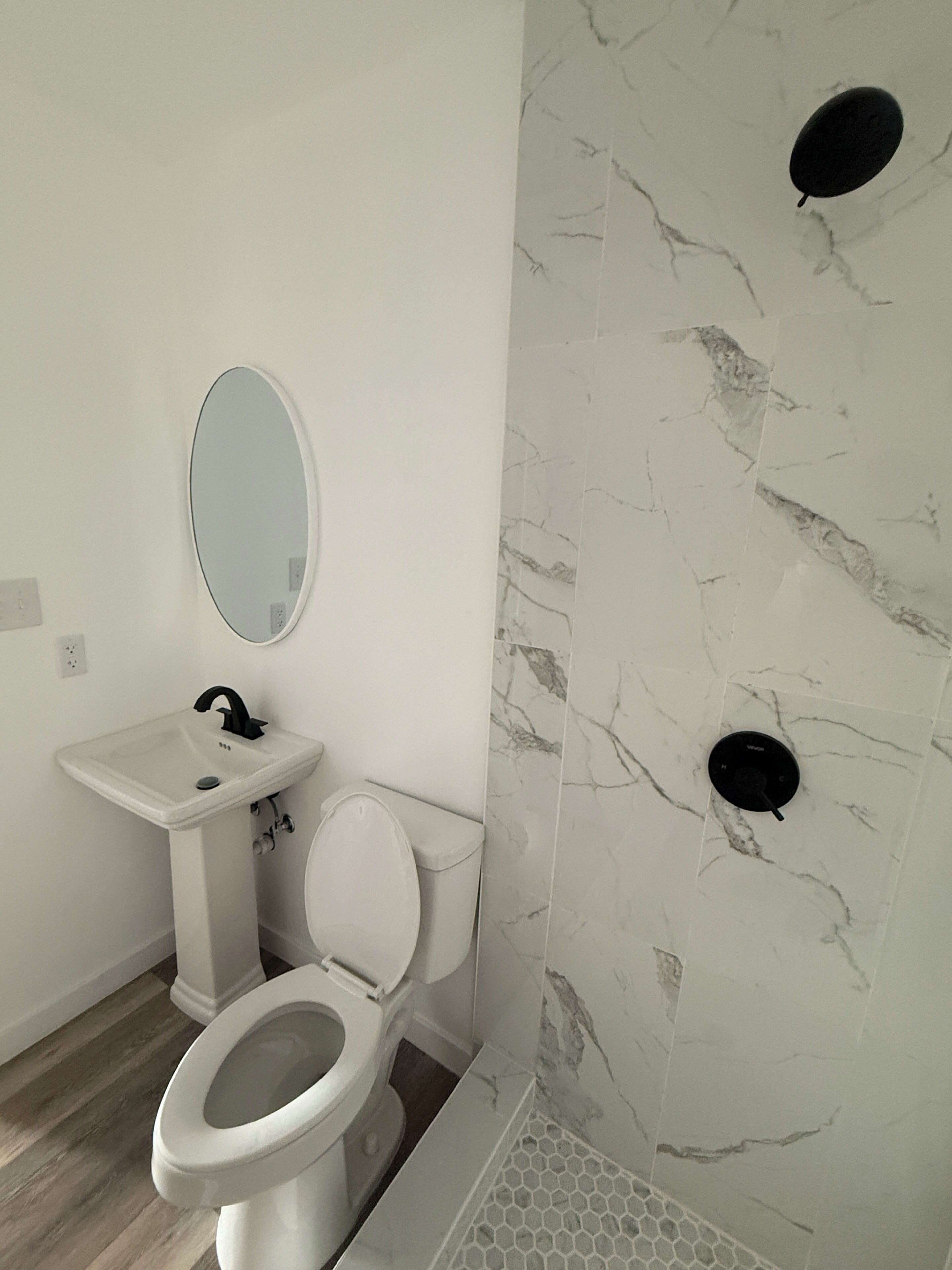 Un baño con inodoro, lavamanos, espejo y pared de mármol.