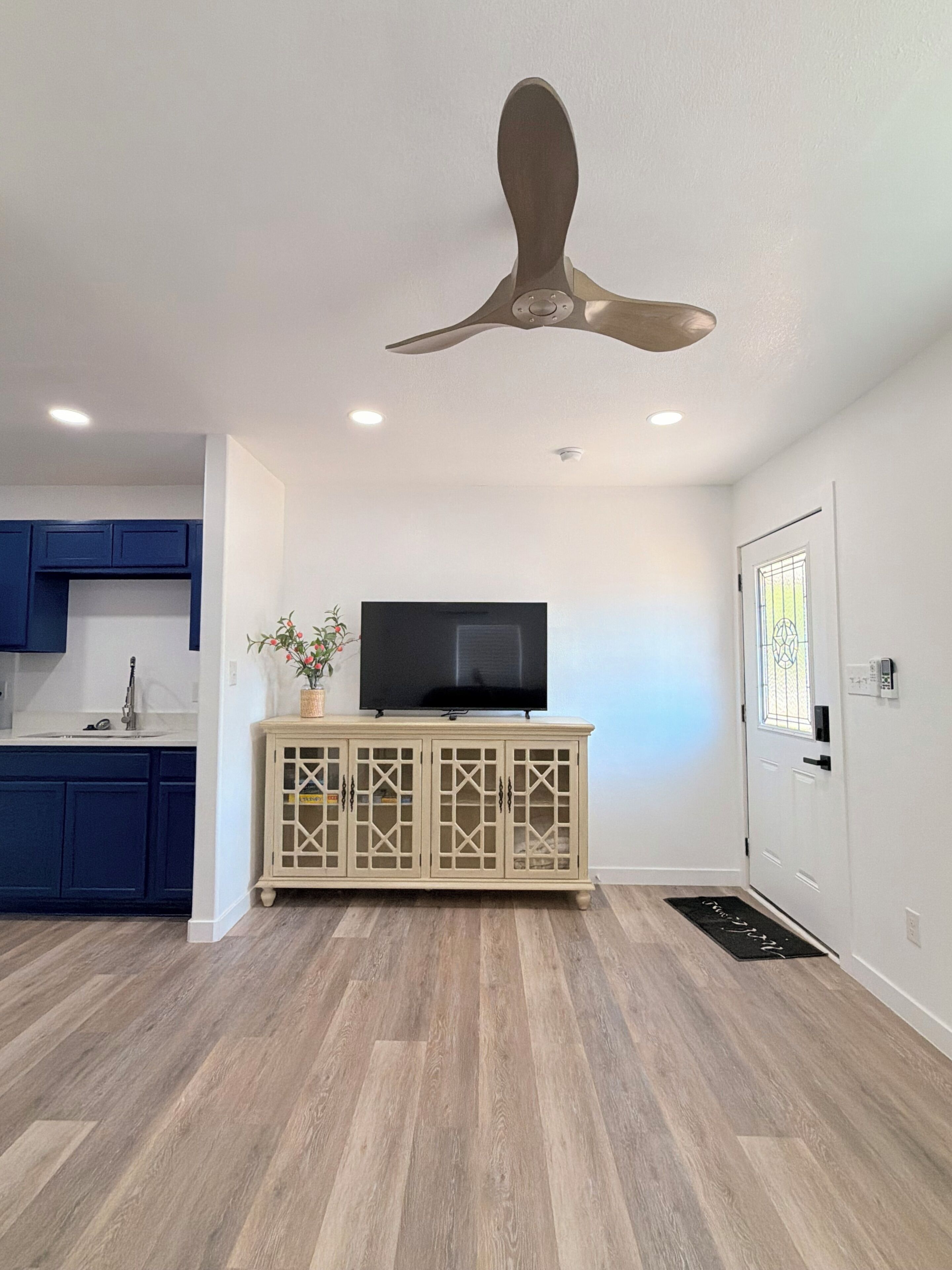 Eine moderne Küche mit blauen Schränken, Holzboden, Deckenventilator und Fernseher auf einem Schrank.