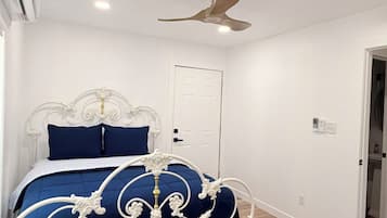A bedroom with a white metal bed frame, a blue bedspread, and a ceiling fan.