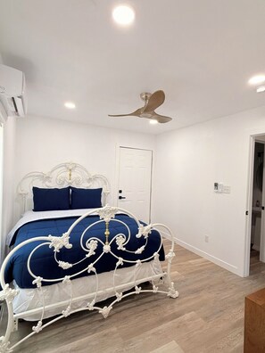 A bedroom with a white metal bed frame, a blue bedspread, and a ceiling fan.