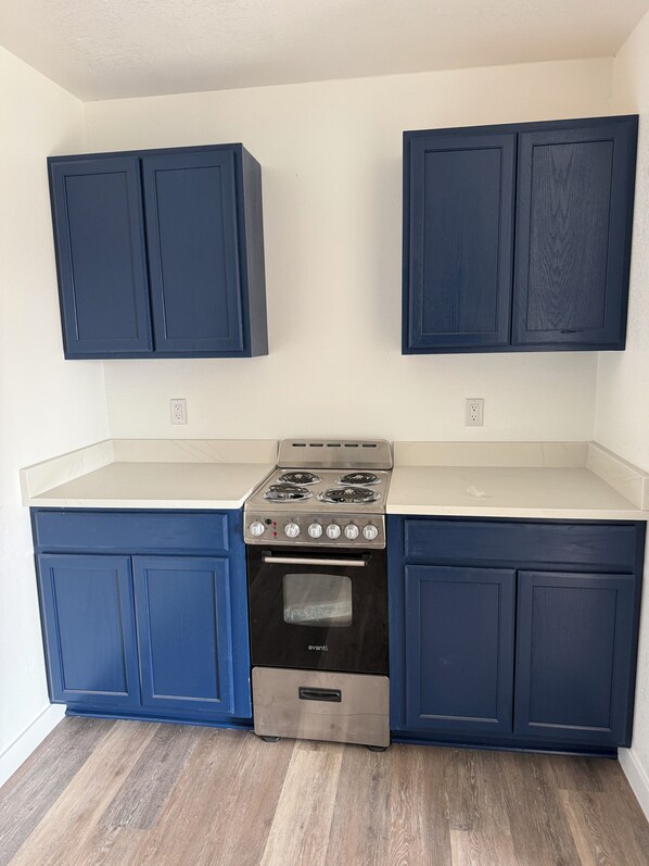 A kitchen with dark blue cabinets, a stainless steel stove, and a white countertop.