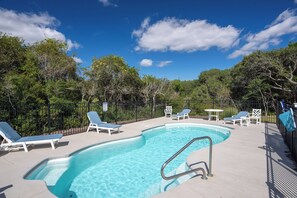 Ein Swimmingpool mit Liegestühlen und einem umzäunten Bereich, umgeben von Bäumen.