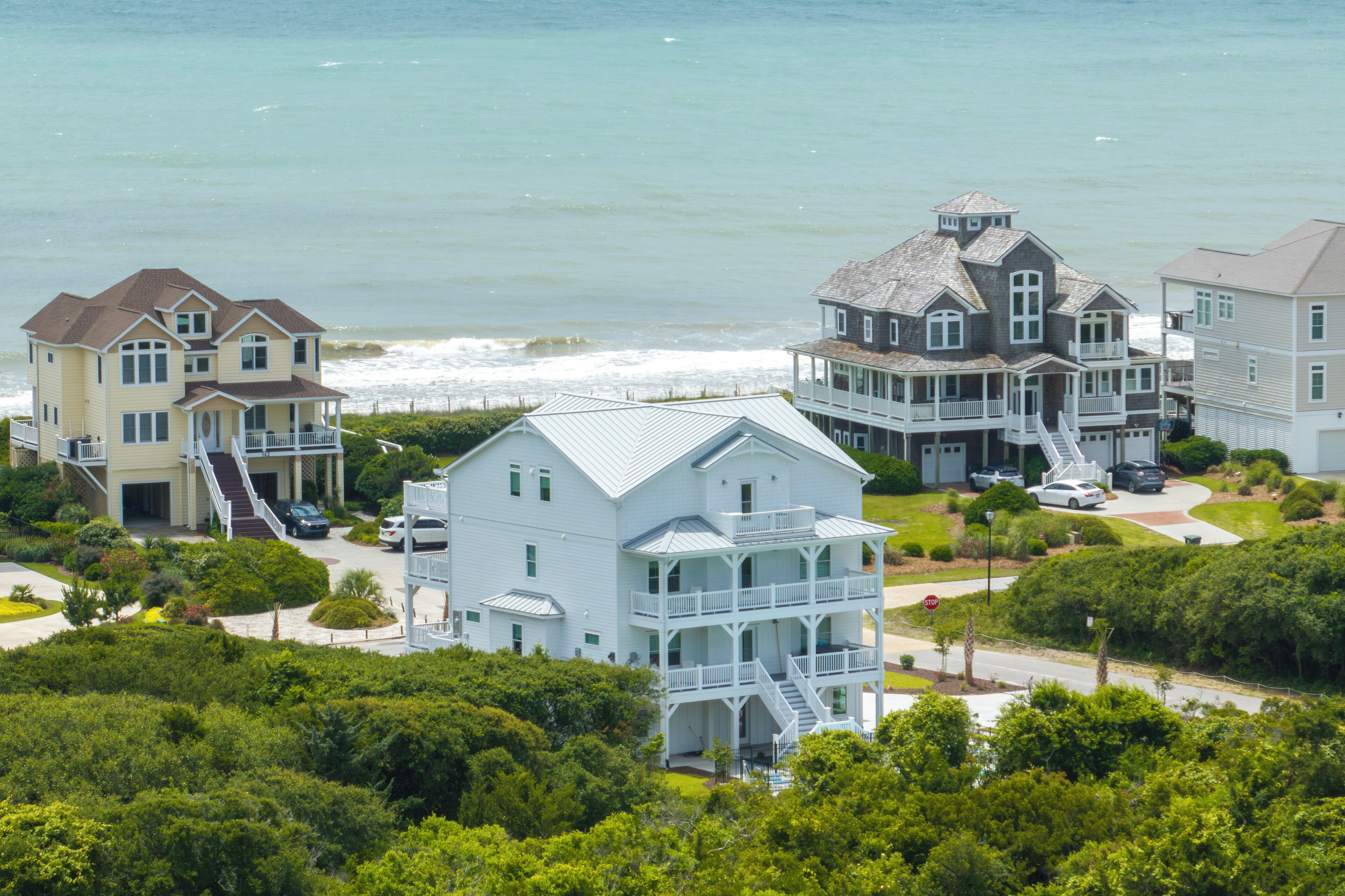 A coastal residential area with multiple houses, including a prominent white house with a balcony and a grey house with a porch.