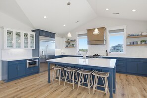 A modern kitchen with a central island, bar stools, and built-in appliances. - Poolside retreat for large groups (North Topsail Beach)