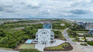 A large white house with a blue balcony, surrounded by lush greenery and a swimming pool. - Poolside retreat for large groups (North Topsail Beach)