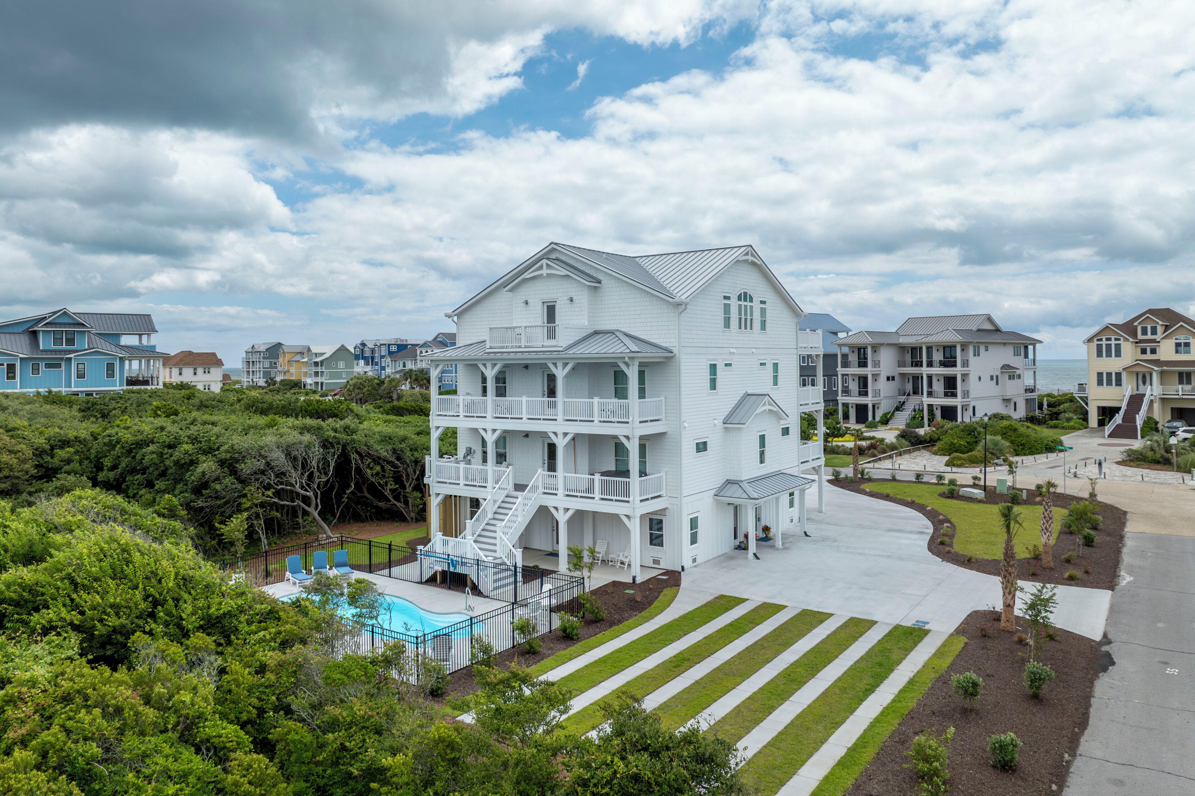 A multi-story white building with a pool, surrounded by greenery and other residential structures.