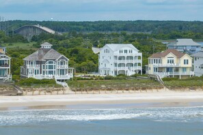 A beachfront property with multiple houses, a beach in the foreground, and a forested hill in the background. - Poolside retreat for large groups (North Topsail Beach)