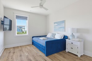 Ein Schlafzimmer mit Bett, Nachttisch, Deckenventilator, Fenster und einem Bild an der Wand.