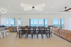 A spacious kitchen with a dining area, large windows, and a view of the ocean. - Oceanfront pool retreat for large groups (North Topsail Beach)