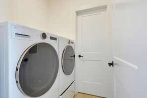 A laundry room with two front-loading washing machines and a white door. - Oceanfront pool retreat for large groups (North Topsail Beach)