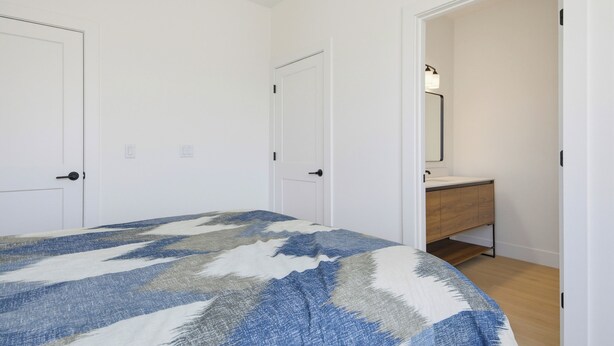 Ein Schlafzimmer mit einem Bett, zwei Türen, einem Badezimmer mit Spiegel und Holzboden.