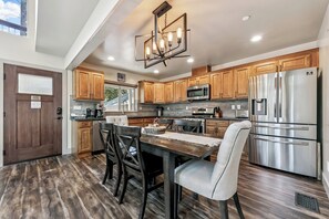 A modern kitchen with wooden cabinets, stainless steel appliances, and a dining area with a table and chairs. - Heavenly Tahoe Escape: EV Charger, BBQ, Balcony (South Lake Tahoe)
