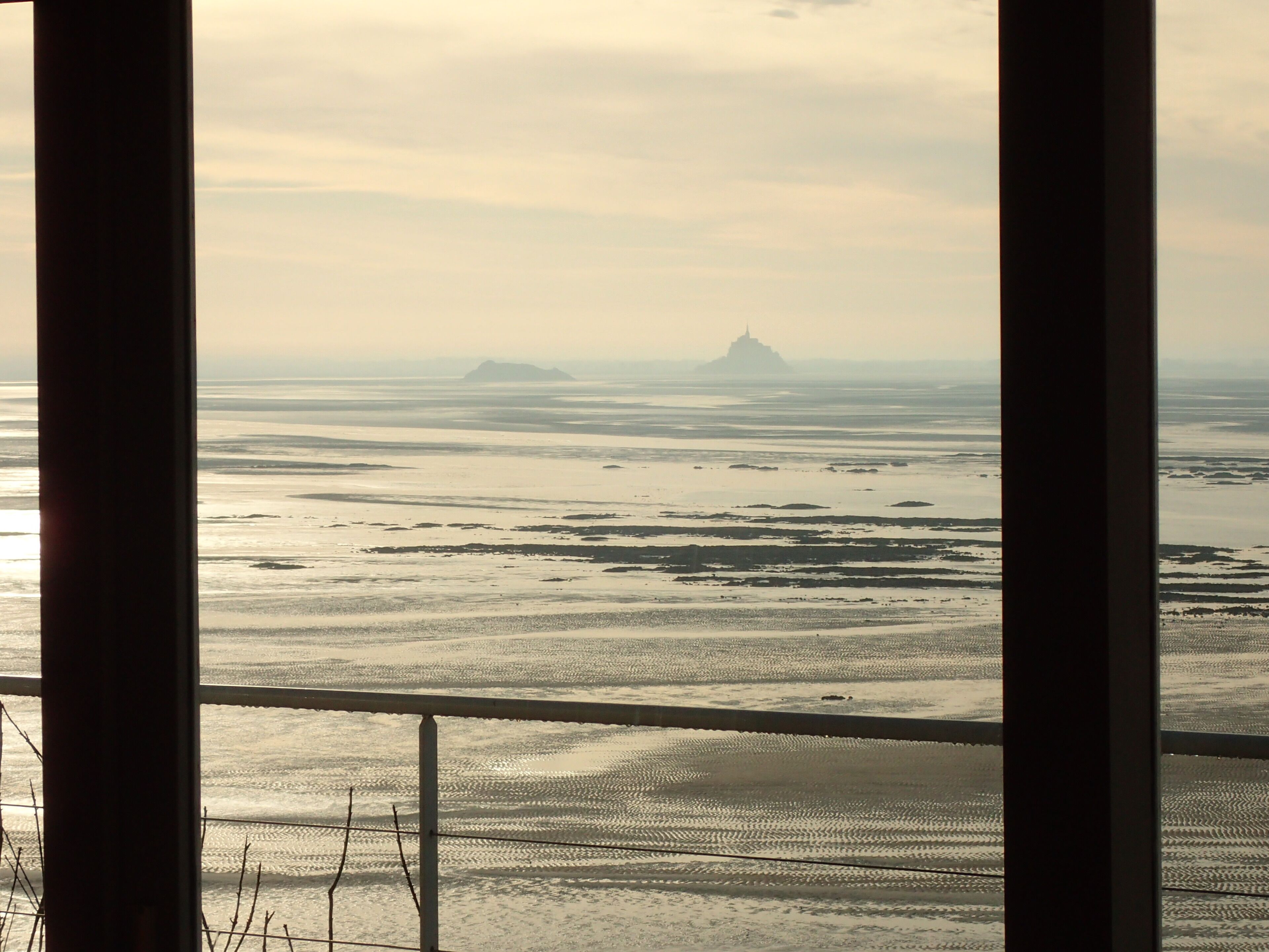 A view through a window with a railing, overlooking a flat landscape with distant landforms.