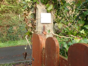 Une porte en métal rustique, agrémentée d’une plaque blanche fixée à un mur, le tout entouré de verdure.