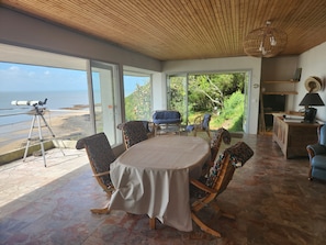 A room with a dining table, chairs, a telescope, and a view of the beach. - Charming 2-bedroom house  face the sea,  magical stay in calm nature (Champeaux)