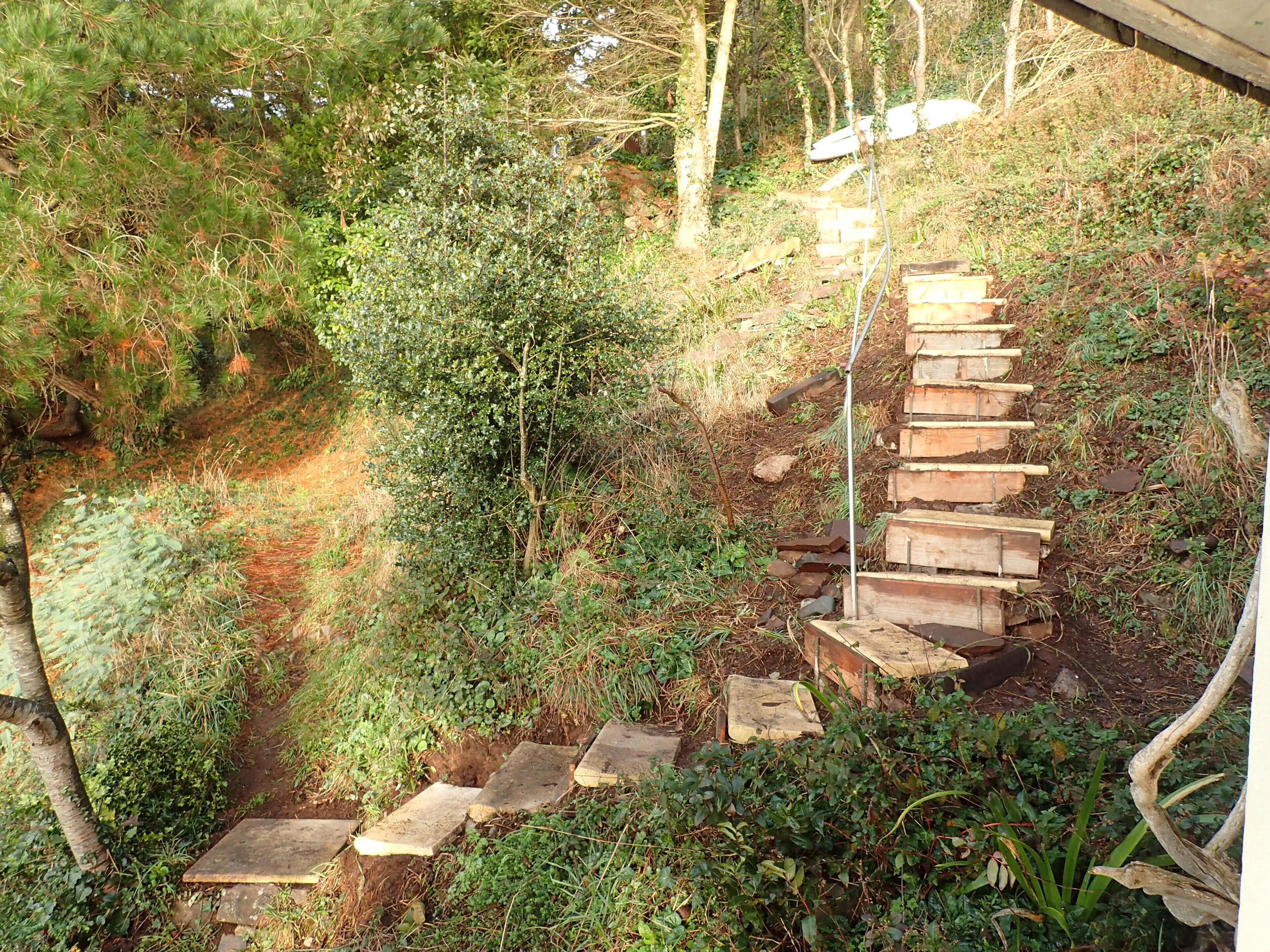 Un escalier en bois menant au sommet d’une colline, entouré de verdure et d’arbres.