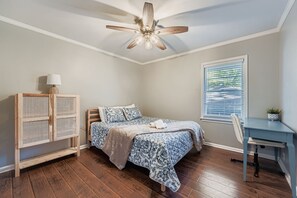 A bedroom with a bed, a desk, a chair, a ceiling fan, and a window with blinds. - Experience Modern Comfort at The Pink Magnolia House (Decatur)