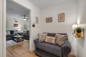 A living room with a grey sofa, a coffee table, and a wall-mounted lamp. - Osceola's Oasis-Townhome with 3 bedrooms and 2.5 bathrooms. Walk to FSU/DOAK. (Tallahassee)
