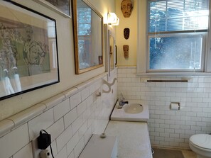 A bathroom with white tiled walls, a sink, a toilet, and framed artwork above the mirror. - Masters Rental: 3-bedroom house 1 block to Press Headquarters 1 mile to course (Augusta)