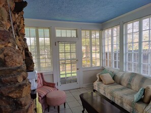 A room with a stone wall, a patterned sofa, a striped chair, and a round ottoman. - Masters Rental: 3-bedroom house 1 block to Press Headquarters 1 mile to course (Augusta)
