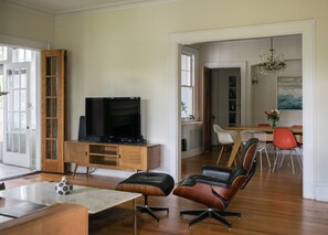 A spacious living room with a television on a wooden cabinet, a dining area with a chandelier, and a view through an open door. - Masters Rental: 3-bedroom house 1 block to Press Headquarters 1 mile to course (Augusta)