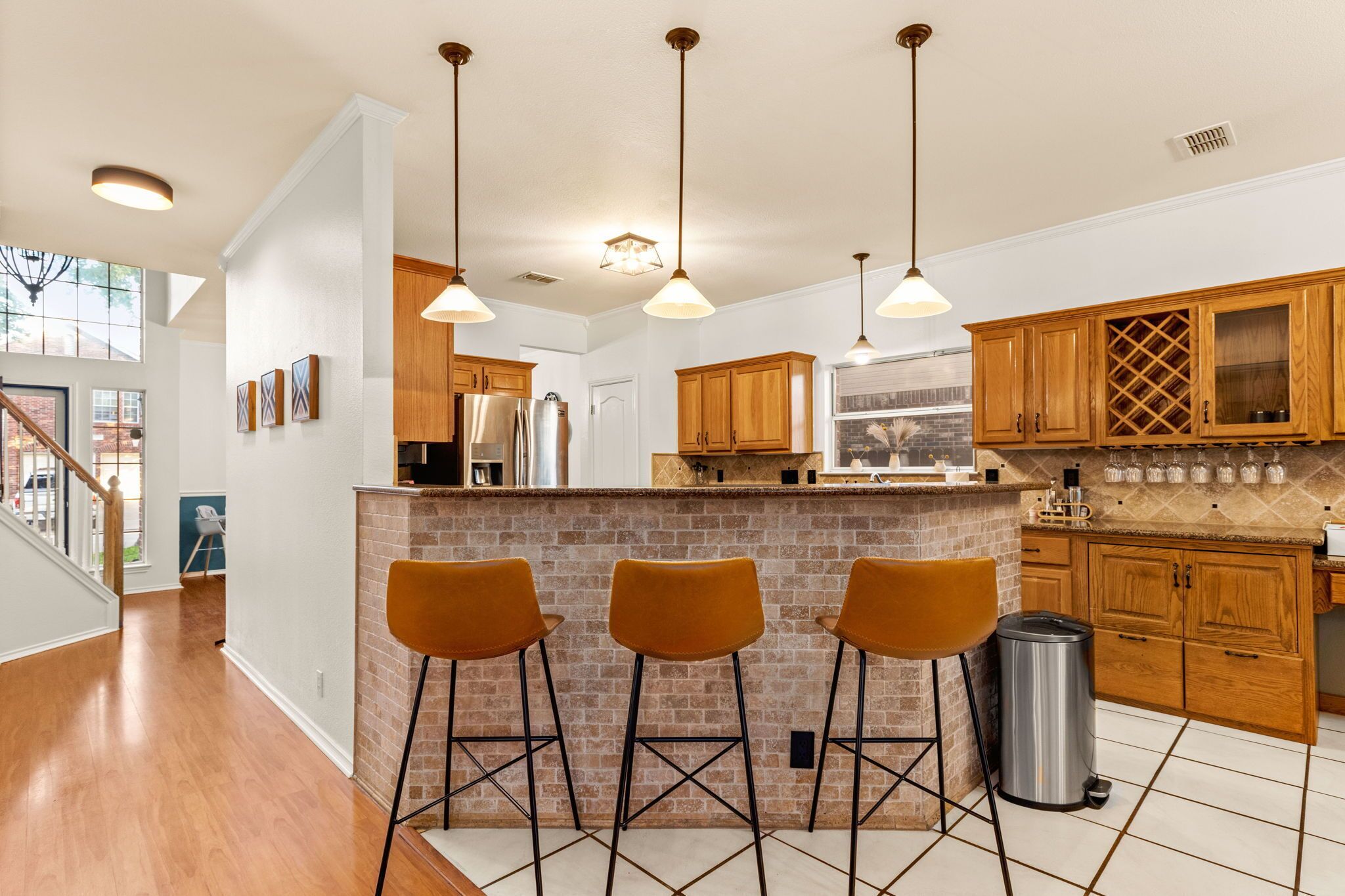 A modern kitchen with wooden cabinets, a brick island, and three bar stools.