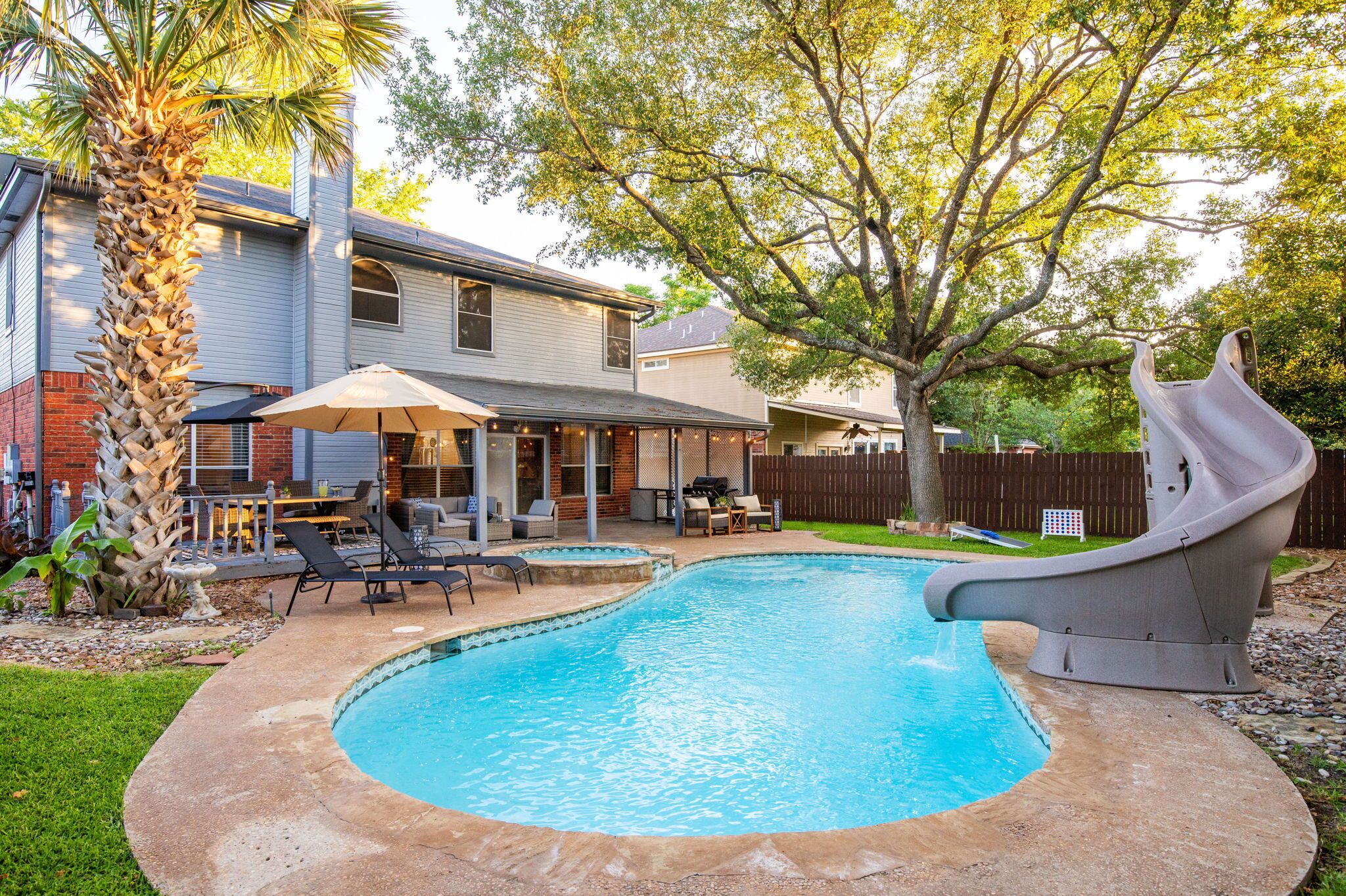 Un jardin avec une piscine, un toboggan, du mobilier d’extérieur et une maison.
