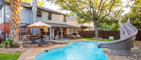 Un patio trasero con piscina, tobogán, muebles de exterior y una casa.