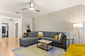 A modern living room with a grey sectional sofa, a wooden coffee table, and a patterned wall. - Family Fun, Heated Pool, Slide, Hot Tub, Game Room (San Antonio)