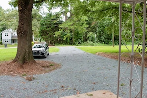 Ein Schotterweg führt zu einem verschlossenen Eingang mit einem Baum links und einem geparkten Auto.