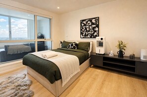 A modern bedroom with a large bed, a window with a view, a wall-mounted artwork, and a bedside table with a heater and a vase. - Wembley Park 1BR 2 Min Tube Gym, Co-Working & Cinema (London)
