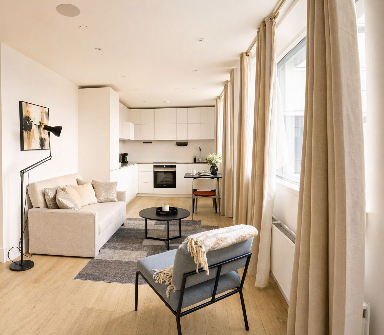 A modern living room with a sofa, a coffee table, and a chair. There is a kitchen area in the background with cabinets and a stove.