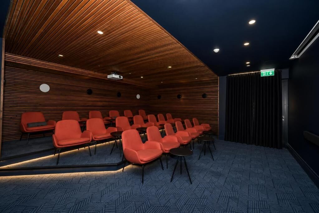 Una sala conferenze con file di sedie, un soffitto in listelli di legno e pavimento rivestito di moquette.