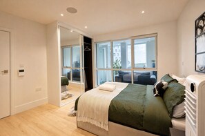 Een moderne slaapkamer met een groot bed, een inloopkast en stadszicht door grote ramen.